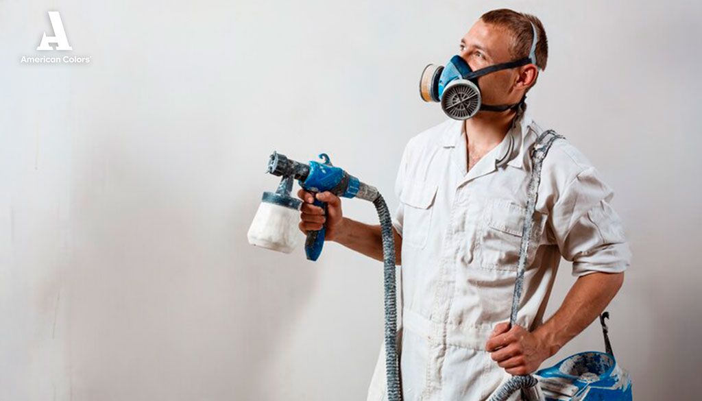 Pintor profesional con equipo de protección aplicando pintura para exteriores con pistola, asegurando un acabado duradero en superficies.