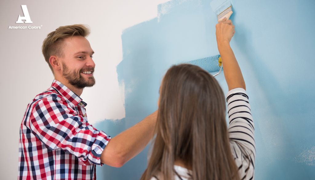 Pareja usando pintura azul con atributos de American Colors Pareja pintando una pared de color azul aprovechando los atributos de American Colors