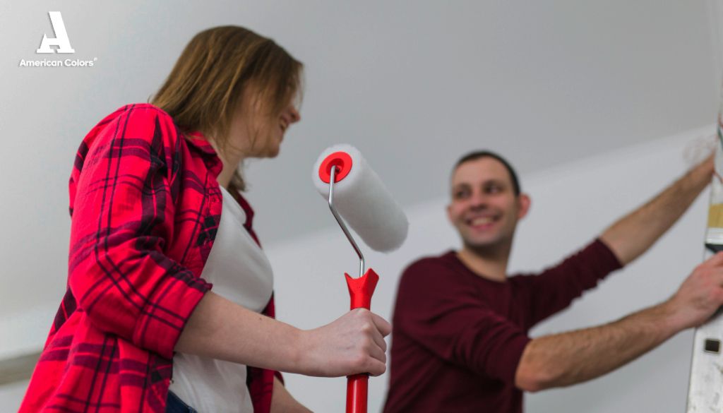 Pareja sonriente pintando una pared probando colores para cocinas con un rodillo, mostrando la alegría y colaboración
