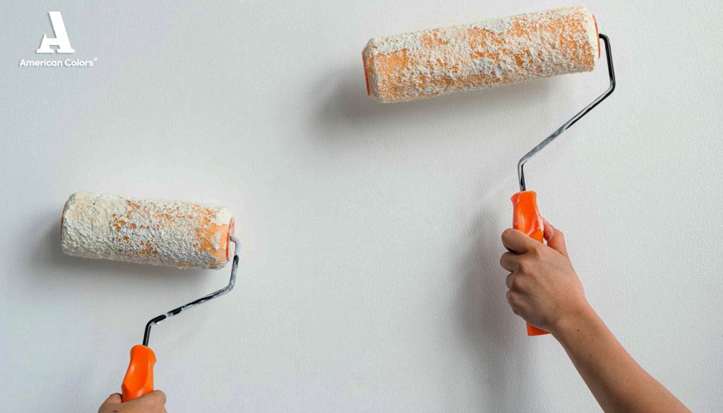 Aplicación de pintura blanca con rodillos a una pared. Dos personas pintando una pared blanca con rodillos de pintura con mangos naranjas.