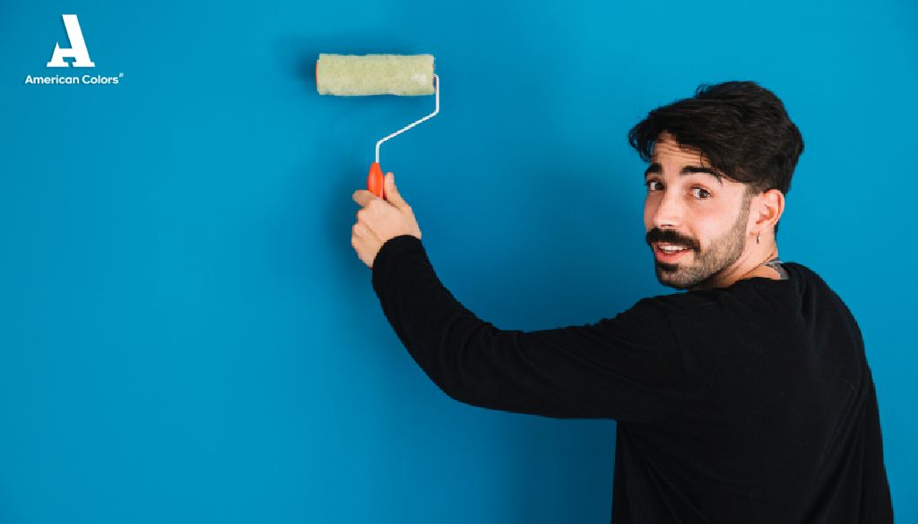 Hombre sonriente pintando una pared azul, con resultado limpio en el que destacan los atributos American Colors